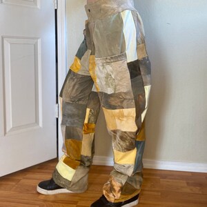 K&ouml;nnte beinhalten: Patchworkhose in den Farbt&ouml;nen Beige, Braun und Gelb. Die Hose hat eine hohe Taille und ein weites Bein. Der Stoff scheint eine Mischung aus Texturen zu sein, mit einer Vielzahl von quadratischen und rechteckigen Flicken, die zusammengen&auml;ht sind. Die Hose wird mit schwarzen Turnschuhen getragen.