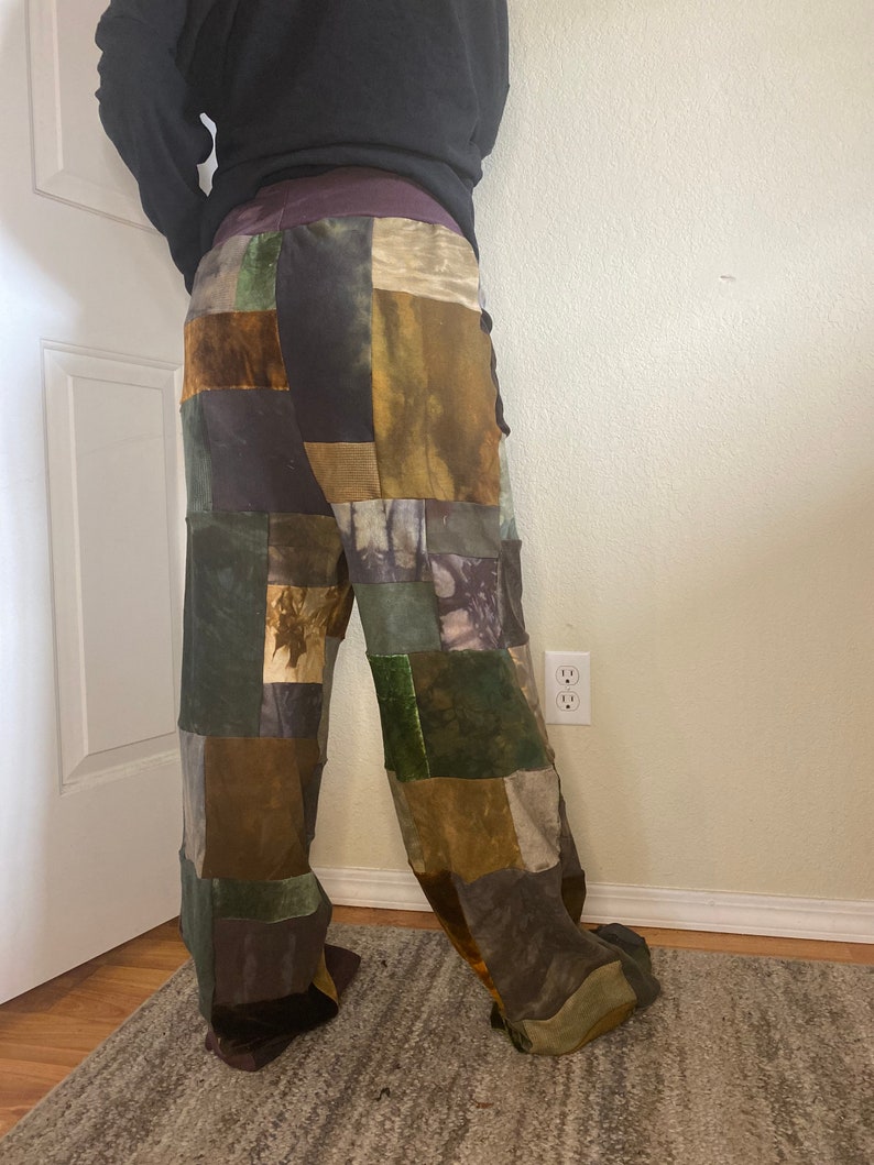 K&ouml;nnte beinhalten: Patchworkhose in Gr&uuml;n-, Braun- und Lilat&ouml;nen. Die Hose besteht aus verschiedenen Stoffquadraten, die zusammengen&auml;ht sind. Die Taille ist einfarbig lila. Die Hose hat weite Beine.