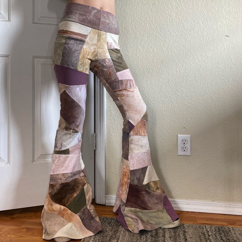 Op de afbeelding: High-waisted broek met uitlopende pijpen en een patchwork-ontwerp bestaande uit verschillende stoftexturen en kleuren, waaronder tinten bruin, beige, mauve, olijfgroen en cr&egrave;me. Het kledingstuk heeft een aansluitende taille en loopt onderaan uit.