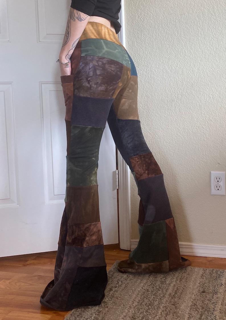 Op de afbeelding: Patchwork broek met uitlopende pijpen, gemaakt van diverse aardetinten in bruin, olijfgroen, antraciet en beige. De broek heeft een hoge taille, wijd uitlopende pijpen en zichtbare zijzakken, opgebouwd uit verschillende panelen met diverse texturen.