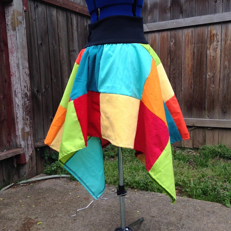 K&ouml;nnte beinhalten: Ein bunter Patchwork-Rock mit einem schwarzen Bund. Der Rock besteht aus verschiedenen farbigen Stoffquadraten, darunter Rot, Orange, Gelb, Gr&uuml;n und Blau.