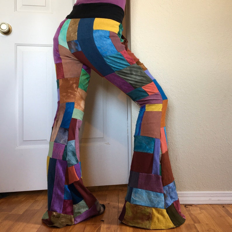 Op de afbeelding: Broek met uitlopende pijpen en een patchworkontwerp met diverse rechthoekige stukken stof in tinten blauw, geel, bruin, groen, paars en oranje. De broek heeft een brede zwarte tailleband en een wijd uitlopend silhouet met zichtbare naden.