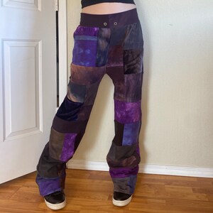 K&ouml;nnte beinhalten: Patchwork-Hose in Lila-, Braun- und Graut&ouml;nen. Die Hose hat einen hohen Bund mit zwei Metall&ouml;sen und eine lockere, bequeme Passform. Der Stoff scheint eine Mischung aus Samt und anderen Materialien zu sein, wodurch eine einzigartige Textur entsteht.