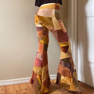 Op de afbeelding: High-waisted broek met uitlopende pijpen en een patchwork-ontwerp bestaande uit verschillende stoftexturen en kleuren, waaronder tinten mosterdgeel, gebrand oranje, donkerbruin, beige en gedempt roze in een geometrische constructie.