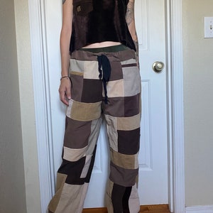 May include: A brown velvet tank top with a small pocket and patchwork pants in shades of brown, tan, and beige. The pants have a drawstring waist and a wide-leg design. The outfit is casual and bohemian.