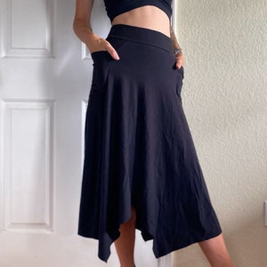 Peut inclure: Un ensemble noir composé d'un crop top épaules nues et d'une jupe midi asymétrique assortie avec des poches. La jupe a un ourlet en mouchoir fluide. La tenue est faite d'un tissu sombre et doux. La personne porte des talons noirs à lanières.