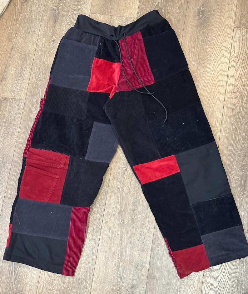Puede incluir: Pantalones patchwork de pernera ancha, con una mezcla de tejidos negros, rojos y grises. Los pantalones tienen cintura con cord&oacute;n y una variedad de texturas, incluyendo pana y terciopelo. Una prenda &uacute;nica y elegante.