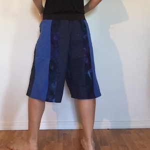 May include: Knee-length shorts in blue and navy, featuring vertical panels. The shorts have a dark blue waistband and a relaxed fit. Some panels have a tie-dye effect. Suitable for casual wear, these shorts are a comfortable garment.