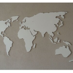 Puede incluir: Un mapa del mundo recortado en blanco, montado en una pared beige. El mapa es un simple contorno de los continentes y oc&eacute;anos.