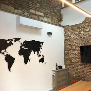 Puede incluir: Un mapa del mundo recortado en negro sobre una pared blanca en un espacio de oficina moderno. El mapa est&aacute; montado en la pared y es un elemento decorativo de la habitaci&oacute;n. Hay una pared de ladrillo en el fondo y una mesa de madera con sillas.
