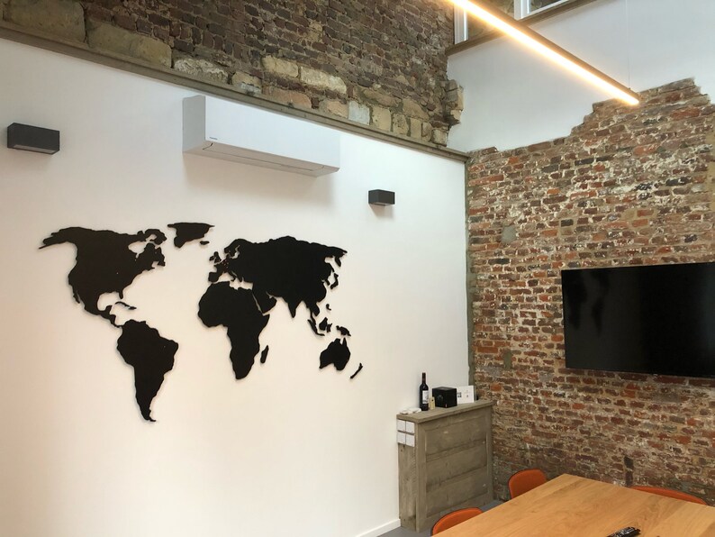 Puede incluir: Un mapa del mundo recortado en negro sobre una pared blanca en un espacio de oficina moderno. El mapa est&aacute; montado en la pared y es un elemento decorativo de la habitaci&oacute;n. Hay una pared de ladrillo en el fondo y una mesa de madera con sillas.