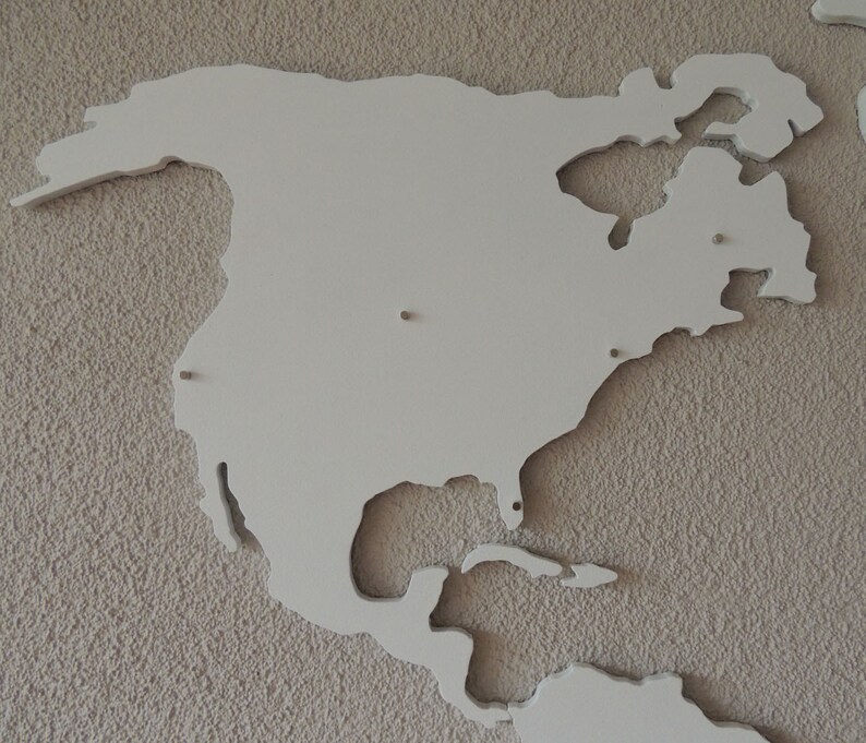 Puede incluir: Un recorte de madera blanco de Am&eacute;rica del Norte, montado en una pared beige texturizada. El recorte es una representaci&oacute;n simplificada del continente, con las principales masas terrestres y algunas de las islas circundantes.