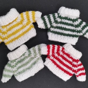 May include: Four miniature knitted sweaters in different colour combinations: yellow and white, green and white, green and white, and red and white.