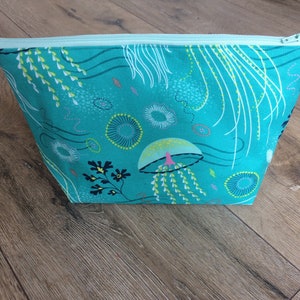 May include: A turquoise zippered pouch with a colorful jellyfish and seaweed pattern. The pouch is made of fabric and has a zipper closure.