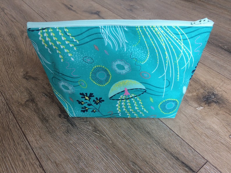 May include: A turquoise zippered pouch with a colorful jellyfish and seaweed pattern. The pouch is made of fabric and has a zipper closure.
