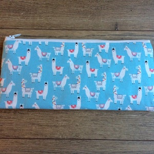 May include: A blue zippered pouch with a white llama pattern. The llamas are wearing colorful saddles.
