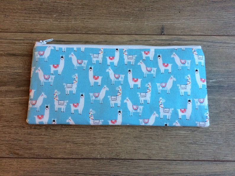 May include: A blue zippered pouch with a white llama pattern. The llamas are wearing colorful saddles.
