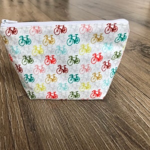 Könnte beinhalten: Weiße Reißverschlusstasche mit einem sich wiederholenden Muster aus bunten Fahrrädern. Die Fahrräder sind in verschiedenen Schattierungen von Rot, Gelb, Grün, Blau und Rosa.