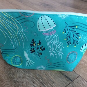 May include: A turquoise zippered pouch with a sea life print. The print features jellyfish, seaweed, and other ocean creatures in shades of green, pink, and yellow.