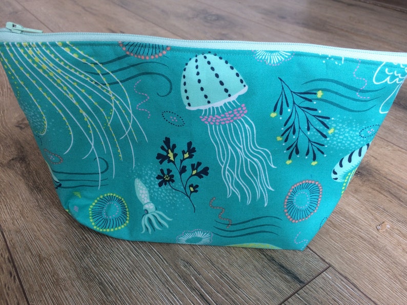 May include: A turquoise zippered pouch with a sea life print. The print features jellyfish, seaweed, and other ocean creatures in shades of green, pink, and yellow.