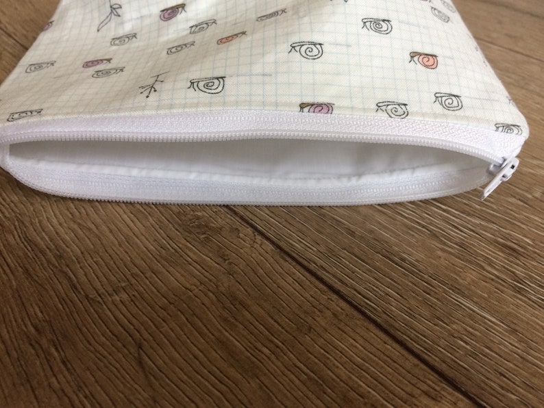 Pu&ograve; includere: Una pochette bianca con cerniera e fodera bianca. Il tessuto ha un motivo a griglia ed &egrave; decorato con un motivo ripetitivo di piccole lumache disegnate a mano.