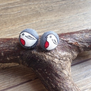 May include: A pair of gray fabric earrings with a red-breasted robin design.