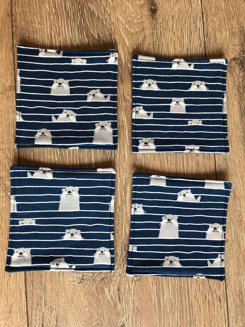 K&ouml;nnte beinhalten: Set mit vier blauen und wei&szlig;en Stoffuntersetzern mit einem Muster aus wei&szlig;en Ottern auf einem blau-wei&szlig; gestreiften Hintergrund.