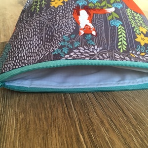 May include: A gray zippered pouch with a teal zipper and a colorful fox print. The print features orange foxes, green leaves, and yellow flowers.