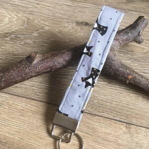 May include: A gray fabric keychain with a black and gold star pattern. The keychain has a silver metal ring.