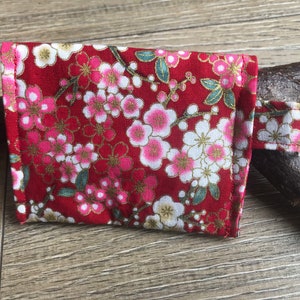 以下が含まれることがあります： 花柄の赤い小さな布製のポーチ。ポーチには白いジッパーと白いストラップが付いています。