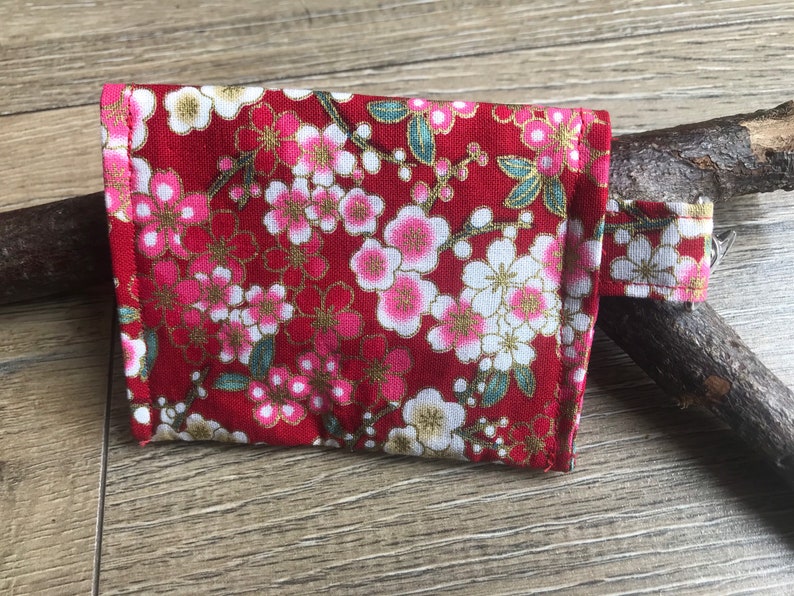 以下が含まれることがあります： 花柄の赤い小さな布製のポーチ。ポーチには白いジッパーと白いストラップが付いています。