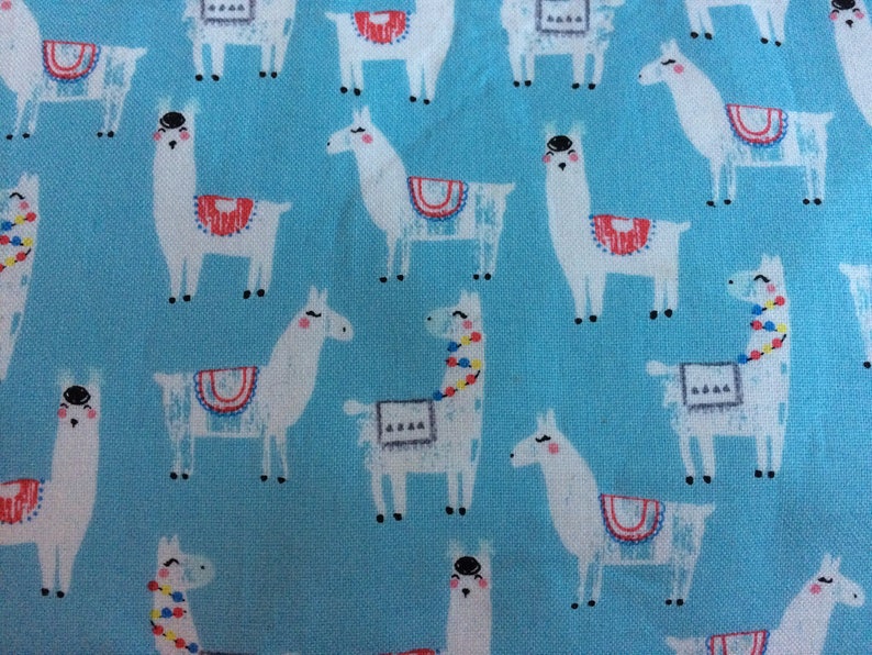 May include: A blue fabric with a repeating pattern of white llamas. The llamas have colorful details on their saddles and some have colorful beads around their necks.