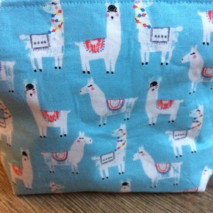 May include: A blue fabric tote bag with a repeating pattern of white llamas with colorful accents. The llamas are wearing saddles and have different colored headbands.