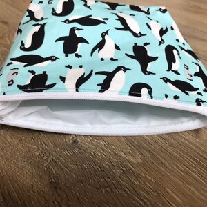 May include: A light blue zippered pouch with a white zipper and a repeating pattern of black penguins on a light blue background.