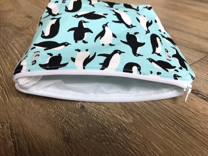 May include: A light blue zippered pouch with a white zipper and a repeating pattern of black penguins on a light blue background.