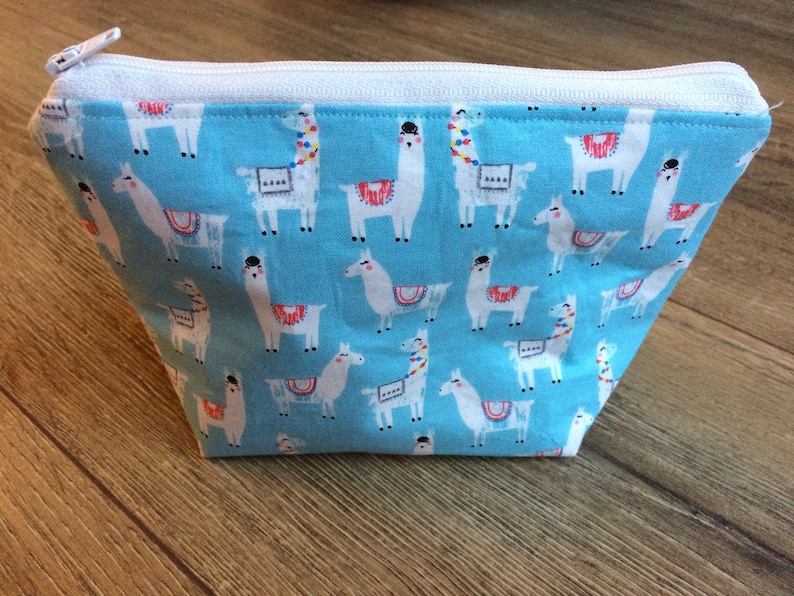 May include: A light blue zippered pouch with a white zipper and a repeating pattern of white llamas on a blue background.