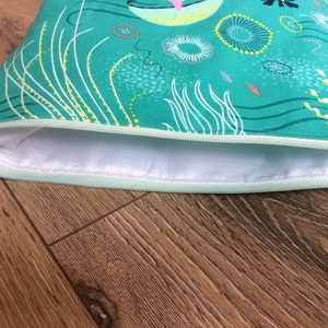 May include: A teal zippered pouch with a white lining. The pouch has a whimsical design featuring white and yellow lines, circles, and swirls.