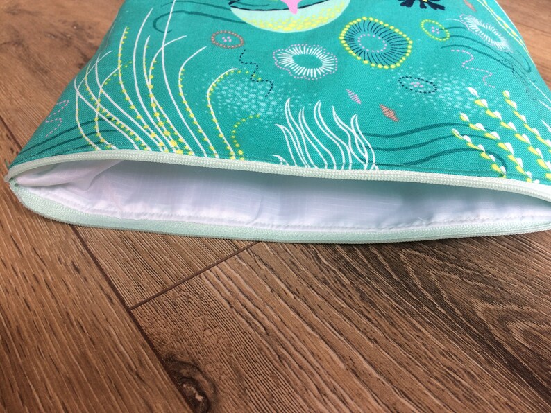 May include: A teal zippered pouch with a white lining. The pouch has a whimsical design featuring white and yellow lines, circles, and swirls.
