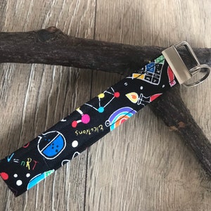 May include: A black and white key chain with a colorful science themed pattern. The pattern includes atoms, molecules, and the words "electrons" and "v=nRT".