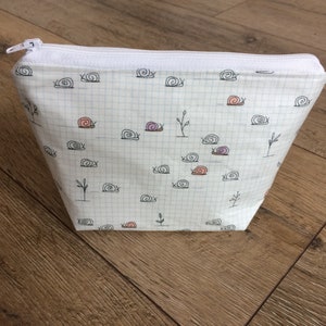 Pu&ograve; includere: Borsa bianca con cerniera, con un motivo a griglia bianco e nero e un motivo ripetuto di lumache nere con conchiglie rosa e viola.