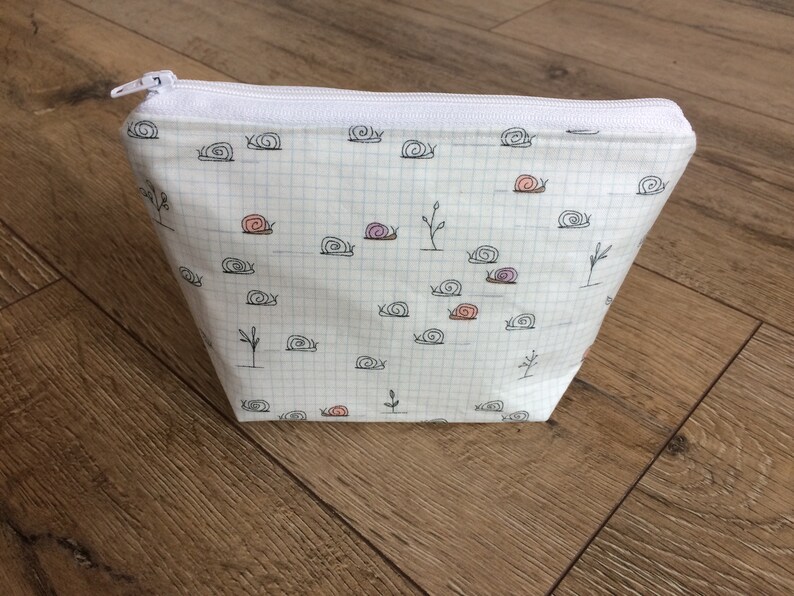 Pu&ograve; includere: Borsa bianca con cerniera, con un motivo a griglia bianco e nero e un motivo ripetuto di lumache nere con conchiglie rosa e viola.