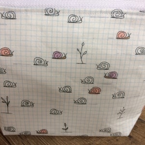 Pu&ograve; includere: Una pochette bianca con cerniera, con un motivo a griglia e un design ripetitivo di lumache nere. Alcune delle lumache hanno conchiglie rosa o viola.