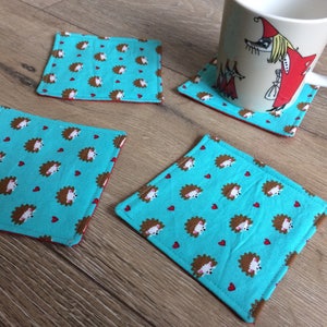 Pu&ograve; includere: Quattro sottobicchieri blu turchese con un motivo di ricci marroni e cuori rossi. I sottobicchieri sono in tessuto e hanno un bordo rosso.