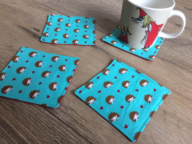 Pu&ograve; includere: Quattro sottobicchieri blu turchese con un motivo di ricci marroni e cuori rossi. I sottobicchieri sono in tessuto e hanno un bordo rosso.