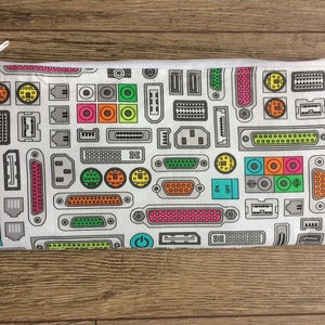 Op de afbeelding: Een witte ritszak met een kleurrijk patroon van computerconnectoren en printplaat elementen. Het patroon bevat verschillende kleuren zoals rood, groen, blauw, geel en oranje.