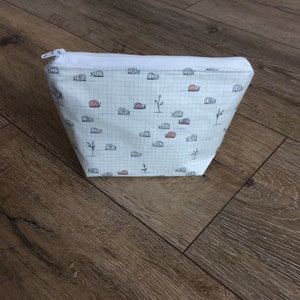 Pu&ograve; includere: Borsa bianca con cerniera, motivo a griglia e un motivo ripetitivo di piccole lumache nere.