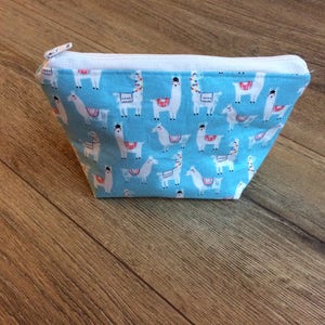 May include: A light blue zippered pouch with a white zipper and a repeating pattern of white llamas on a blue background.