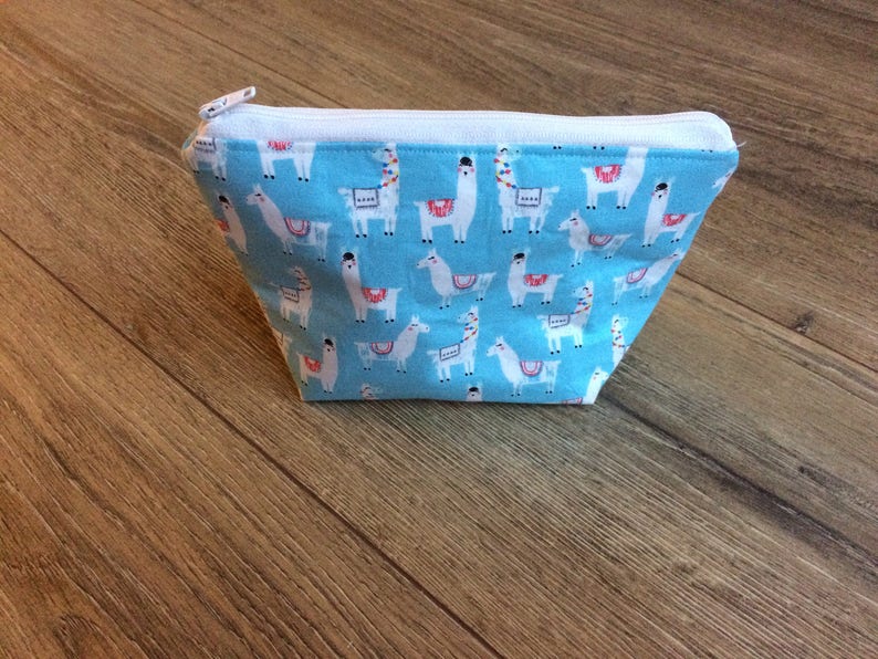 May include: A light blue zippered pouch with a white zipper and a repeating pattern of white llamas on a blue background.