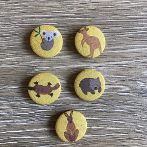 May include: Six round yellow fabric buttons with different Australian animals printed on them. The animals include a koala, kangaroo, platypus, wombat, and a rabbit.
