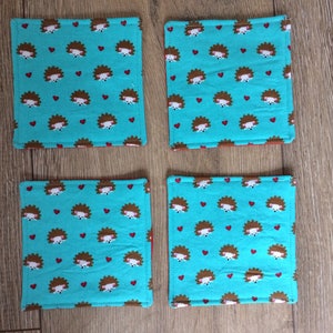 Pu&ograve; includere: Quattro sottobicchieri in tessuto blu turchese con un motivo ripetitivo di ricci marroni e cuori rossi.